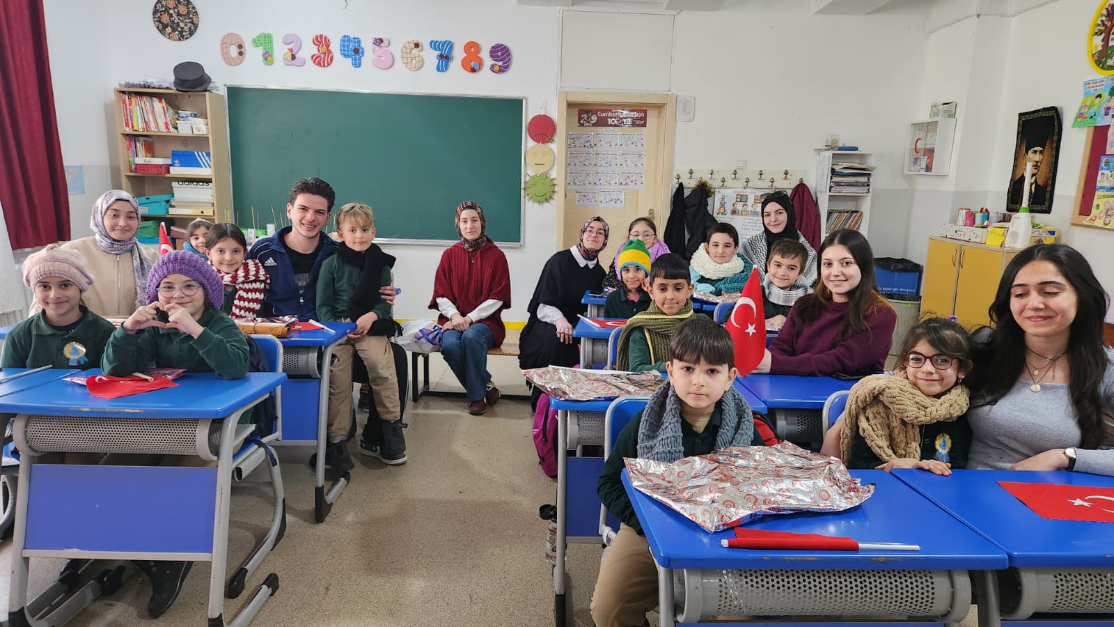 TR: Bir sınıfta sıralarda oturan bir grup öğrenci ve yetişkin birlikte poz veriyor. EN: A group of students and adults posing together at desks in a classroom.