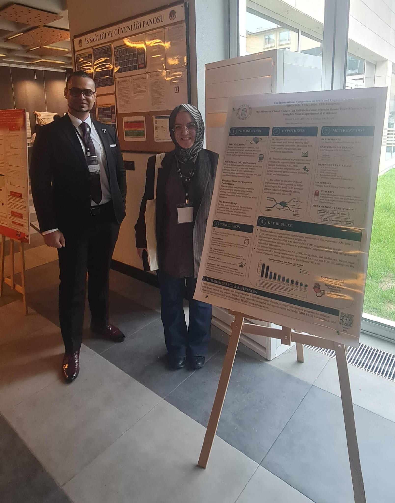 TR: Ghaith Al Badran ve Funda Salman ISBCS 2026 sempozyumunda bilimsel posterin önünde poz veriyor. EN: Ghaith Al Badran and Funda Salman posing in front of a scientific poster at the ISBCS 2026 symposium.